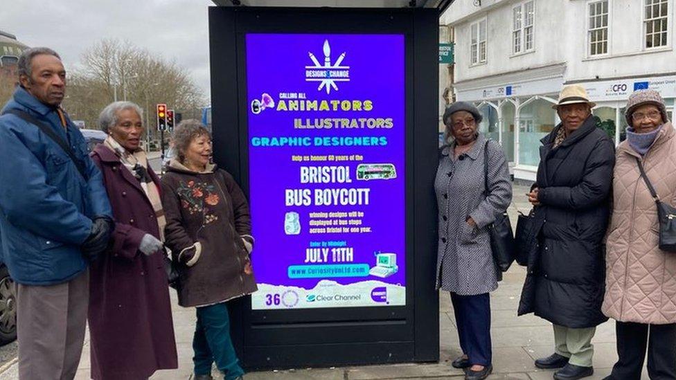 Six people standing next to the bus stop which has a poster advertising the design competition