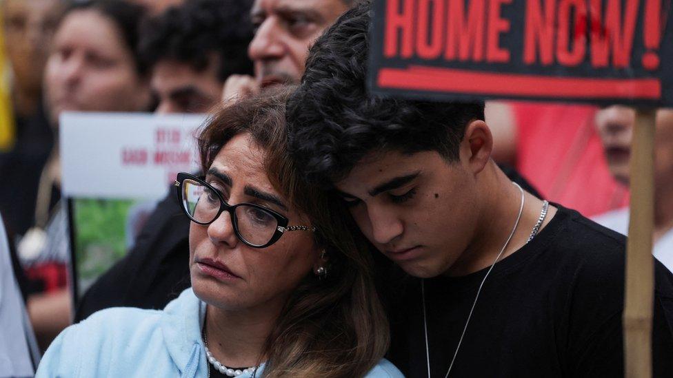 A boy standing beside a woman leans his head against hers