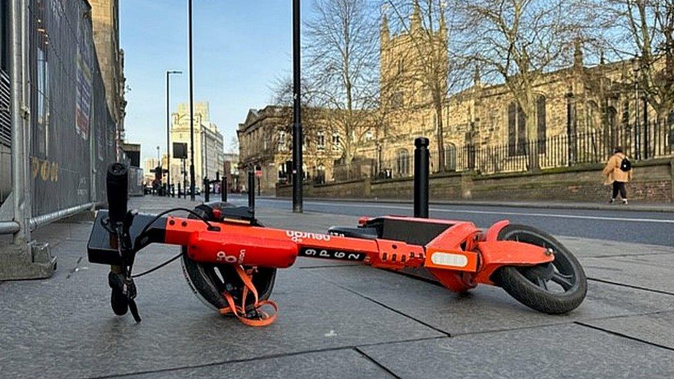 A scooter lying on its side int he middle of the pavements