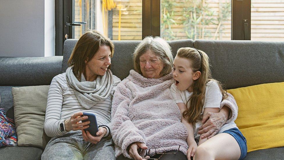 Mother, grandmother and daughter sitting on a sofa looking at a phone