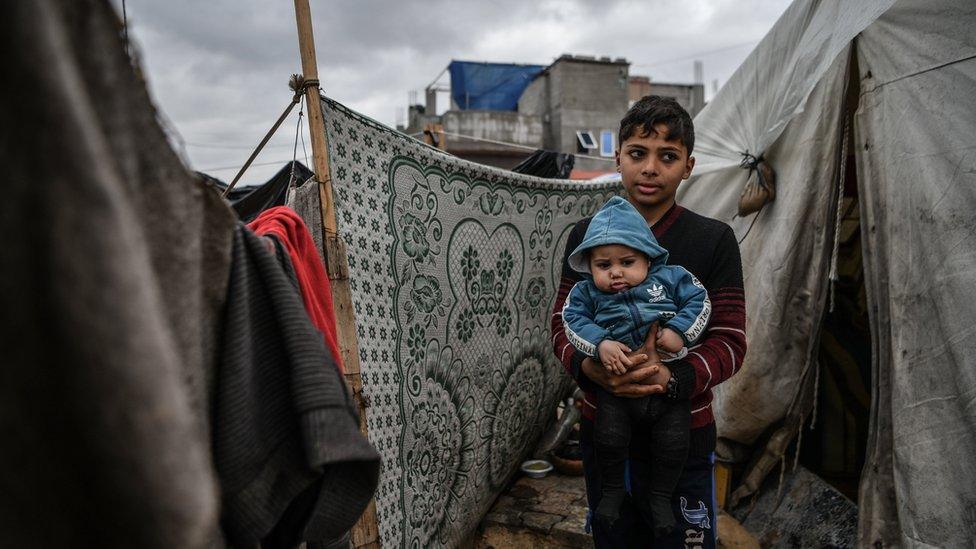 14-year-old boy and six-month-old baby brother outside tent in Rafah