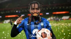 Ademola Lookman célèbre la victoire de l'Atalanta en Europa League en mordant sa médaille tout en tenant le ballon de match.