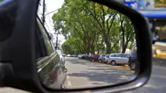 Carros estacionados em via pública vistos no reflexo do espelho retrovisor de um carro