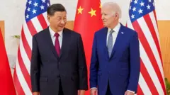 Xi Jinping e Joe Biden em pé em frente a bandeiras, com sorrisos contidos