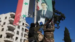 Dois homens com roupas camufladas vistos por trás de um cartaz com a imagem do presidente sírio, Bashar al Assad.