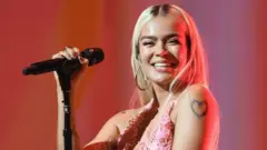 A cantora colombiana Karol G segura um microfone e sorri enquanto se apresenta em um show em Los Angeles