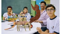 Julia, Guilherme e André exibem seus projetos de robótica na sala de recursos com o professor Edson