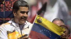 Nicolas Maduro vestindo casaco branco segura bandeira da Venezuela em comício