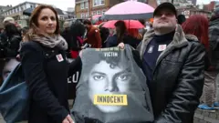 Dois fãs mostram camisa com rosto de Michael Jackson em protesto em defesa ao cantor em frente ao prédio da emissora Channel 4