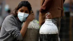 A woman holds on to the oxygen cylinders for a patient after refiling them at a factory, amidst the spread of coronavirus disease (COVID-19) surge as India"s outbreak spreads across South Asia, in Kathmandu, Nepal May 9, 2021.