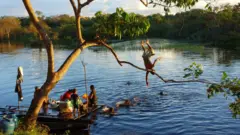 Crianças ribeirinhas brincam no rio enquanto mulheres lavam roupa, em Jutaí (AM)