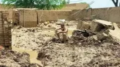 Um idoso sentado no meio de uma casa destruída por inundações