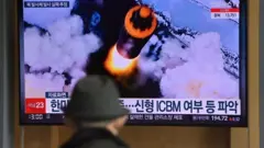 People watch a television screen showing a news broadcast with file footage of a North Korean missile test, at a railway station in Seoul on March 16, 2022