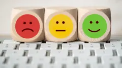 Três cubos de emojis (carinha feliz, triste e sem expressão) em cima de teclado de computador