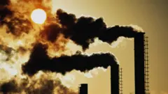 Smoke pluming out of 3 chimneys in front of hazy bright sun