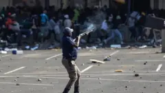 A member of the South African Police Services fires rubber bullets at rioters looting the Jabulani Mall in Soweto, southwest of Johannesburg, on 12 July 2021