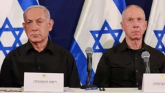 Netanyahu e seu antigo ministro da Defesa, Yoav Gallant, lado a lado; eles são dois homens brancos idosos e há bandeiras de Israel ao fundo 