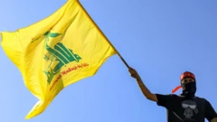 Militante do Hezbollah vestido de camiseta preta e touca vermelha balança banderia do grupo, amarela e com dizeres verdes em árabe 