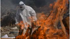 A Family member, wearing a Personal Protective Equipment (PPE), performs the last rites for COVID-19 victims