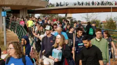 Dezenas de pessoas caminhando em ponte e carregando diversos objetos