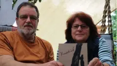 Bernd and Ulla Brammer hold a booklet showing the name of their ancestor 'witch'