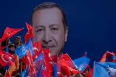 Pessoas e bandeiras em frente a grande painel com foto de Erdogan 