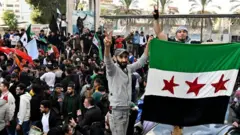 Multidão agitando bandeiras em Damasco após a queda do regime de Assad na Síria