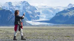 Mulher tira foto de paisagem com montanhas e neve na Islândia