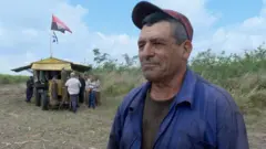 Miguel Guzmán em área de campo, observado por outros homens atrás