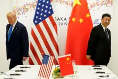 Fotografia colorida mostra Trump, um idoso branco de terno, e Xi Jinping um idoso amarelo de terno, de costas um para o outro ao lado de bandeiras de seus países