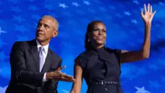 Barack and Michelle Obama gesture and wave while onstage at the DNC in Chicago on 20 August