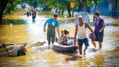 Homens usam bote para resgatar pessoas durante enchents em Porto Alegre