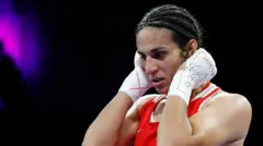 Imane Khalif olha para frente vestindo um uniforme de boxe e luvas