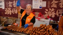 Mulher trabalhando em uma barraca de comida acenando para alguém.