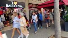 Pessoas caminhando em calçada, com loja chamada 'I love Barcelona' atrás