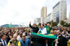 Bolsonaro, Michelle Bolsonaro, o 'veio da Havan' em cima de um carro acenam para pessoas na orla de Baleneário Camboriú