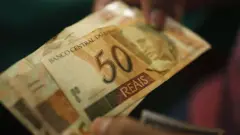 Uma pessoa segura nota de R$ 50 reais 