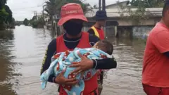 Bombeiro Leandro Simões segura bebê no colo em área alagada