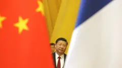 Chinese President Xi Jinping is seen between China and France's national flags in Beijing on January 9, 2018. - Chinese President Xi Jinping and French counterpart Emmanuel Macron met Tuesday for talks and to oversee the signing of business deals as the two global leaders seek closer ties