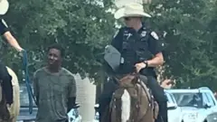 Two officers on horseback leading suspect on foot