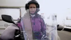 Célia Campos em sua moto, parada em frente ao trailer onde mora