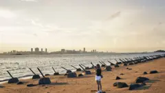 Buildings in Xiamen on mainland China stand across the Taiwan Strait from anti-landing barriers on a beach in Kinmen, Taiwan, on Monday, Aug. 21, 2023.