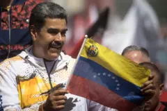 Nicolas Maduro vestindo casaco branco segura bandeira da Venezuela em comício