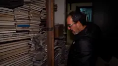 Feras Kilani regarde des piles de livres dans une pièce sombre.