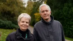 Cheryl e David Essam sorrindo contidamente para foto em parque