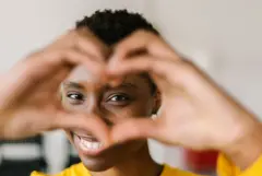 A young woman making a heart shape with fingers in front of her eyes