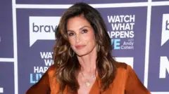 Cindy Crawford, vestida de laranja, olha para a câmera, em foto de julho de 2024