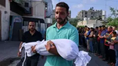 Homem carrega corpo de criança morta no conflito entre Israel e Hamas