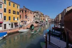 Imagem de barcos sobre canal em Veneza, com casas de cores variadas ao fundo