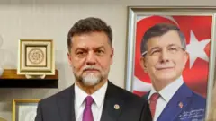 Nedim Yamalı, Ahmet Davutoğlu'nun fotoğrafının yanında duruyor